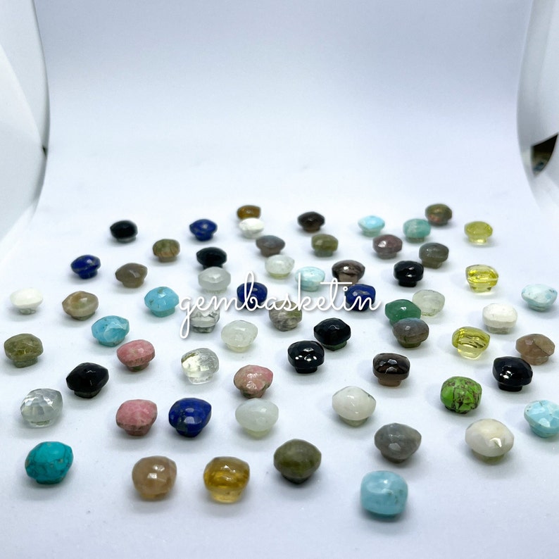 May include: Assortment of small, faceted gemstone cabochons in various colors, including turquoise, green, blue, pink, brown, black, and white. The gemstones are arranged on a white surface. The text "gembasketin" is visible in the center of the image.