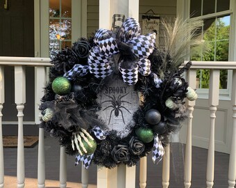 May include: A black and white checkered bow with black and green Halloween decorations on a black wreath. The wreath has a sign that says "Spooky" with a spider on it.
