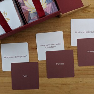 May include: A set of white cards with inspirational questions and red cards with corresponding keywords. The questions include "Where can I put my trust?", "What can I do to make this better?", and "What is my potential?" The keywords include "Faith", "Purpose", "Strength".