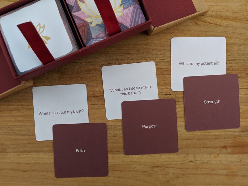 May include: A set of white cards with inspirational questions and red cards with corresponding keywords. The questions include "Where can I put my trust?", "What can I do to make this better?", and "What is my potential?" The keywords include "Faith", "Purpose", "Strength".