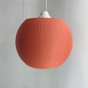 May include: A coral-colored pendant light with a wavy, textured shade. The light is suspended from a white cord.