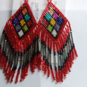 May include: A pair of red beaded earrings with a colorful geometric pattern and black and silver fringe.