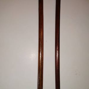 May include: Two wooden dowels, one is a darker brown and the other is a lighter brown.