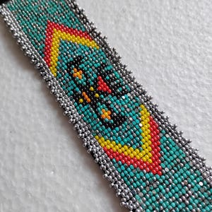 May include: A beaded bracelet with a black backing. The bracelet features a central design in turquoise, red, yellow, and black beads, framed by a border of silver beads. The design is geometric and symmetrical.