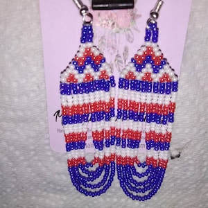 May include: A pair of long, beaded earrings with a red, white, and blue color scheme. The earrings are made with small, round beads and have a fringe-like design at the bottom.