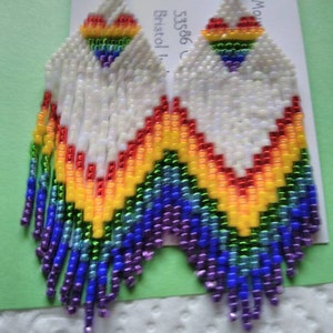 May include: Rainbow heart beaded earrings with a white background. The earrings are made with small, colorful beads and have a fringe design.
