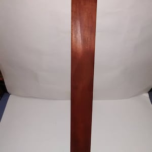 May include: A long, thin, wooden bat with a dark brown stain. The bat is smooth and has a slight curve at the end.