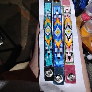K&ouml;nnte beinhalten: Drei Perlenarmb&auml;nder mit geometrischen Mustern in T&uuml;rkis, Blau und Rosa. Jedes Armband hat einen silbernen Druckknopfverschluss.