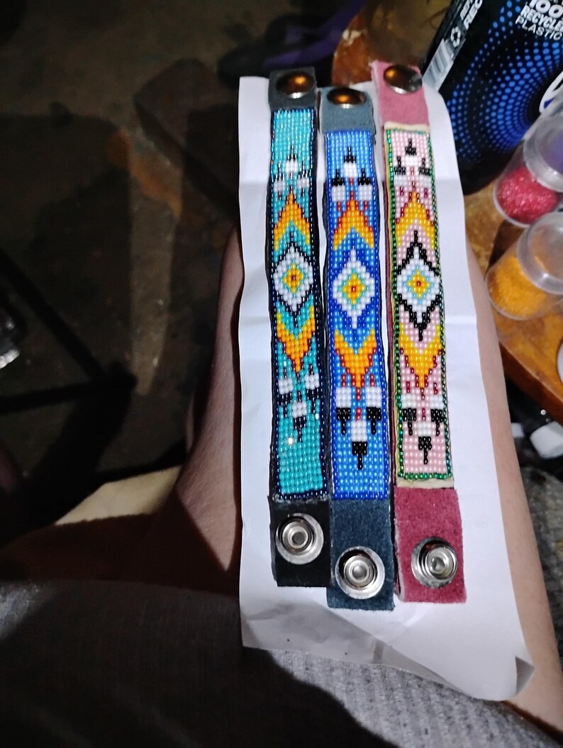 K&ouml;nnte beinhalten: Drei Perlenarmb&auml;nder mit geometrischen Mustern in T&uuml;rkis, Blau und Rosa. Jedes Armband hat einen silbernen Druckknopfverschluss.