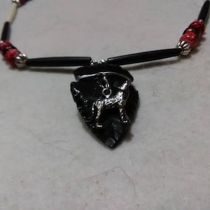 May include: A black and red beaded necklace with a black arrowhead pendant featuring a silver wolf charm.