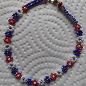 May include: A beaded bracelet with a red, white, and blue flower pattern. The bracelet has a silver clasp.