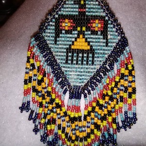 May include: A beaded earring with a geometric design in shades of blue, black, yellow, red, and white. The earring has a fringe of beads in the same colors.