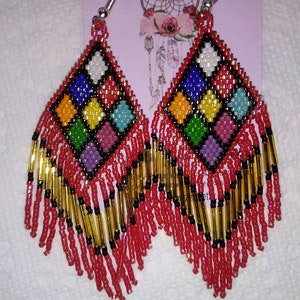 May include: A pair of red beaded earrings with a colorful geometric design and fringe. The earrings are made with red, black, gold, white, blue, green, yellow, and pink beads.