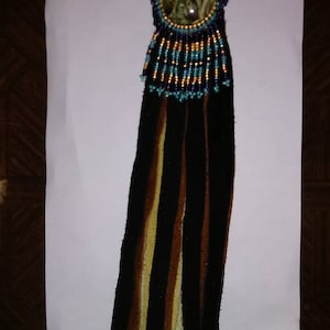 May include: A beaded tassel necklace with a round, brown and white stone pendant. The tassel is made of black, brown, and beige leather strands.