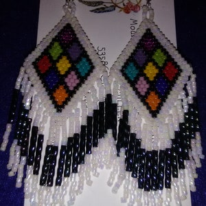 May include: A pair of colorful beaded earrings with a diamond-shaped design and white and black fringe. The earrings are made with small, colorful beads and have a silver-toned hook.