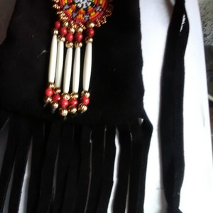 May include: A black leather pouch with a beaded design and fringe. The pouch has a beaded strap and a white bone bead accent.