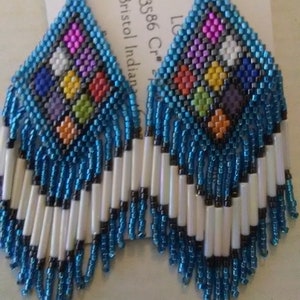 May include: A pair of blue and white beaded earrings with a colorful geometric design in the center. The earrings are made with seed beads and have a fringe.