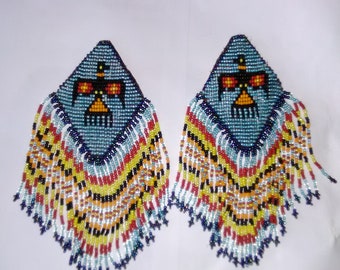 May include: A pair of beaded earrings with a blue, red, yellow, and white color scheme. The earrings are shaped like a teardrop and have a fringe at the bottom.