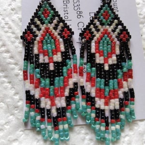 May include: A pair of beaded earrings with a geometric design in black, white, red, and turquoise. The earrings are long and dangle, with a fringe of beads at the bottom.