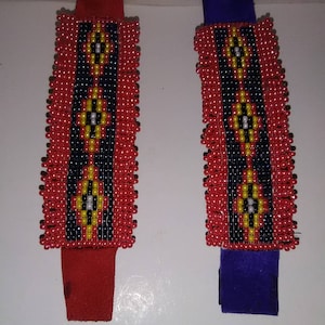 May include: Two beaded bracelets with geometric patterns. One bracelet has a red leather strap and the other has a blue leather strap.