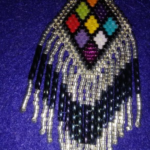 May include: A beaded earring with a geometric design in shades of red, orange, yellow, green, blue, purple, and white. The earring has a fringe of black and silver beads.