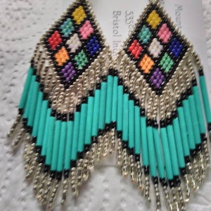 May include: A pair of turquoise and silver beaded earrings with a colorful geometric pattern. The earrings are made with small beads and have a fringe design.