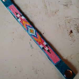 K&ouml;nnte beinhalten: Ein t&uuml;rkisfarbenes Armband mit einem geometrischen Muster in Pink, Gelb, Wei&szlig; und Schwarz.