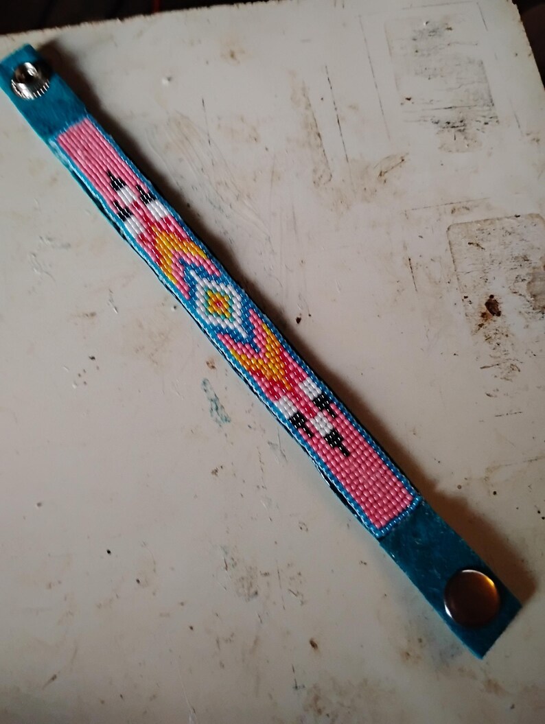 K&ouml;nnte beinhalten: Ein t&uuml;rkisfarbenes Armband mit einem geometrischen Muster in Pink, Gelb, Wei&szlig; und Schwarz.