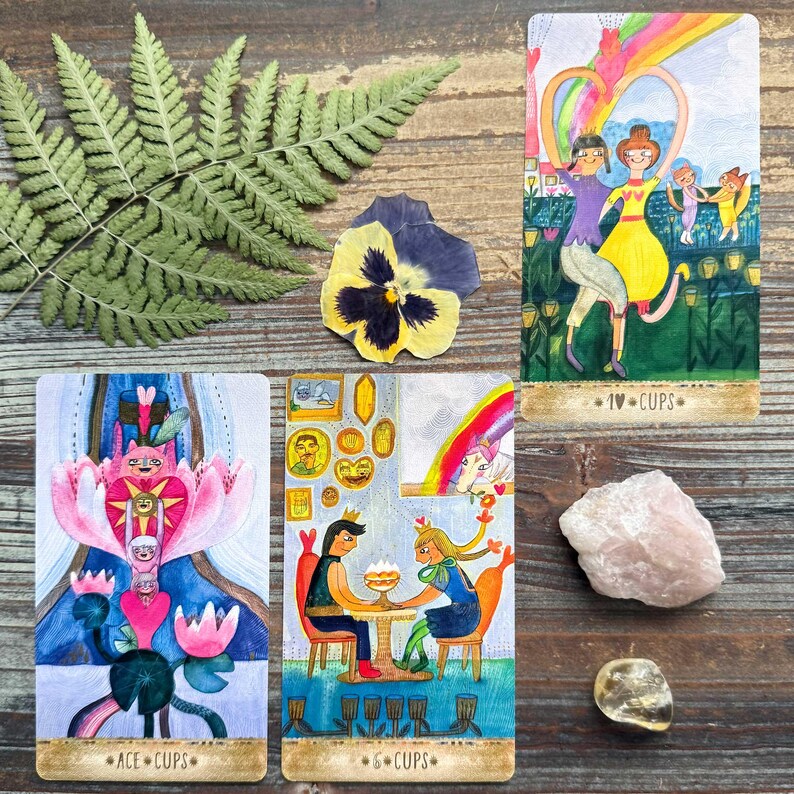 a collection of tarot cards, a fern leaf, and some crystals arranged on a wooden surface.