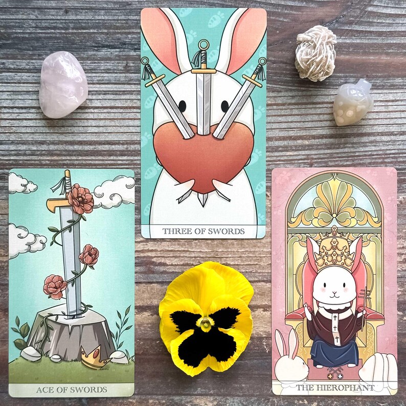 three tarot cards and some crystals arranged on a wooden surface.