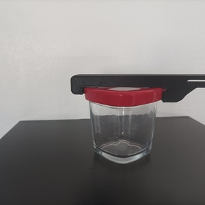 Peut inclure: Un ouvre-bocal en plastique noir avec un couvercle rouge sur un bocal en verre. L'ouvre-bocal est conçu pour ouvrir facilement les bocaux.