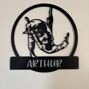 Peut inclure: Décoration murale en métal noir représentant la silhouette de deux personnes en position de combat d'arts martiaux, avec le nom "ARTHUR" inscrit en dessous.