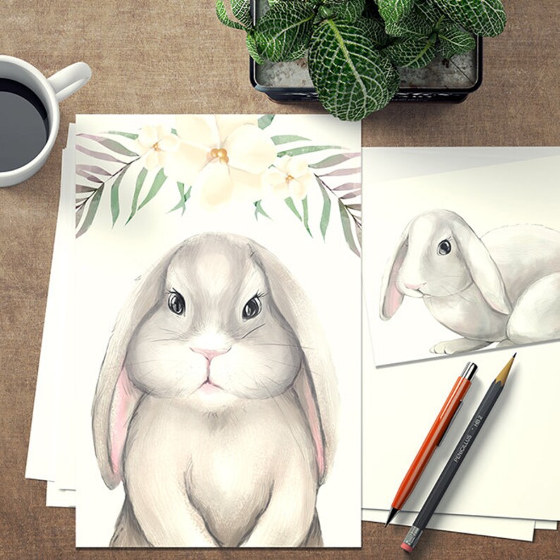 K&ouml;nnte beinhalten: Eine Aquarell-Illustration eines niedlichen grauen Kaninchens mit rosa Ohren. Das Kaninchen ist von wei&szlig;en Blumen und gr&uuml;nen Bl&auml;ttern umgeben.
