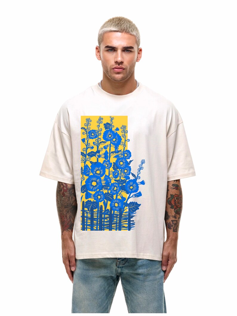 May include: A white t-shirt with a blue and yellow floral print. The print features a fence and flowers in a yellow background.
