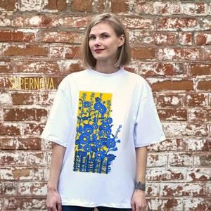May include: White t-shirt with a graphic print of blue flowers in a yellow rectangle. The text "SUPERNOVA" is visible in the top left corner of the image.