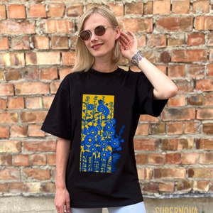 May include: Black t-shirt with a graphic print of blue flowers and a yellow fence. The shirt is oversized and has short sleeves.