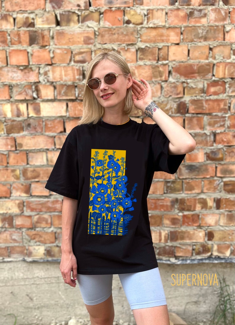 May include: Black t-shirt with a graphic print of blue flowers and a yellow fence. The shirt is oversized and has short sleeves.