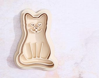 Puede incluir: Un cortador de galletas de madera con forma de gato sentado. El cortador es de color marrón claro y tiene un diseño detallado.