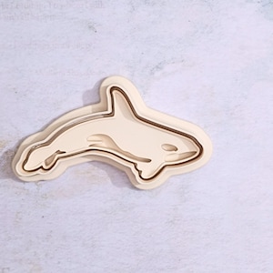 Op de afbeelding: Een witte plastic koekjesvormer in de vorm van een orka. De vormer heeft een dubbellagig ontwerp, met een licht verhoogde buitenrand.