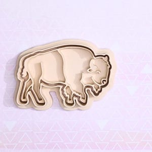 Op de afbeelding: Een beige bisonvormige koekjesuitsteker met een gedetailleerde omtrek en een lachend gezicht. De koekjesuitsteker is gemaakt van plastic en is ontworpen om te bakken. De bizon is een symbool van het Amerikaanse Westen.