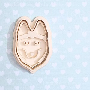 Könnte beinhalten: Ein Holz-Ausstecher in Form eines Husky-Hundegesichts. Der Ausstecher besteht aus zwei Teilen, einem für die Umrandung und einem für die Details des Gesichts.