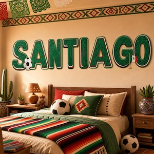 Pode incluir: Grandes letras verdes de parede soletrando SANTIAGO com padrões intrincados, uma pequena bola de futebol anexada à letra S e uma pequena bandeira mexicana na letra G. As letras estão montadas em uma parede bege acima de uma cama.