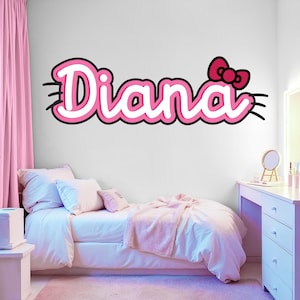May include: A pink and white wall decal that spells out the name "Diana" in a playful font, with a red bow accent. The decal is set against a white wall in a bedroom with pink curtains and bedding.