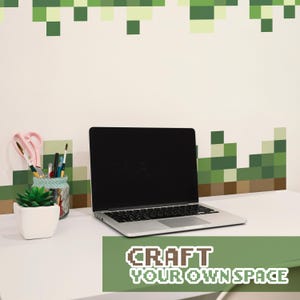 May include: A silver laptop with a black screen sits on a white desk. A small potted succulent, scissors, and pens are nearby. The text "CRAFT YOUR OWN SPACE" is displayed on a green banner.
