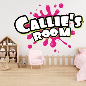 Pode incluir: Um adesivo de parede rosa e verde com o texto "Callie's Room" em branco, em negrito. O adesivo tem a forma de um design de tinta rosa salpicada.