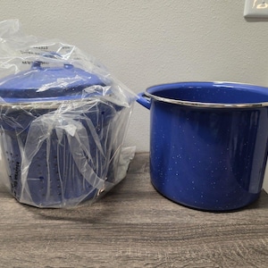 May include: A set of two deep blue enamel pots with white speckled details. One pot is a colander with side handles and a lid, partially wrapped in clear plastic. The second pot is a matching deep blue stockpot with two side handles and a silver rim.