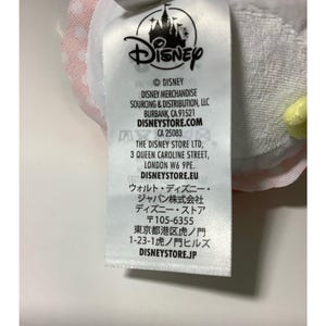 May include: A white tag with the Disney logo and text. The tag includes the Disney copyright information, the address for Disney Merchandise Sourcing & Distribution, and the address for The Disney Store Ltd.