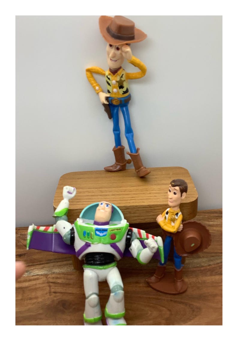 May include: A collection of Toy Story character figurines, including Woody in a cowboy hat and Buzz Lightyear with his wings extended. The figures are brightly coloured and stand on a wooden surface.