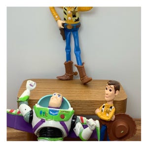 May include: Toy Story character figures of Woody, Buzz Lightyear, and a third character. Woody wears a yellow shirt, blue trousers, and brown boots. Buzz Lightyear is in a green and white spacesuit with purple wings. The third character is in a yellow shirt and brown hat.