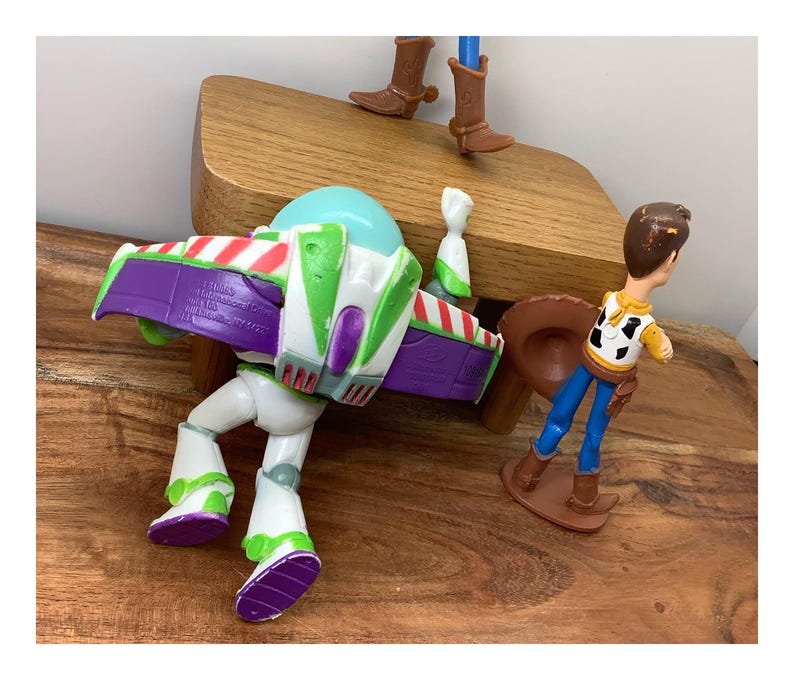 May include: Toy Story character figures of Buzz Lightyear and Woody. Buzz is white, green, purple, and red. Woody wears a yellow shirt, blue trousers, and a brown cowboy hat. The figures are on a wooden surface.